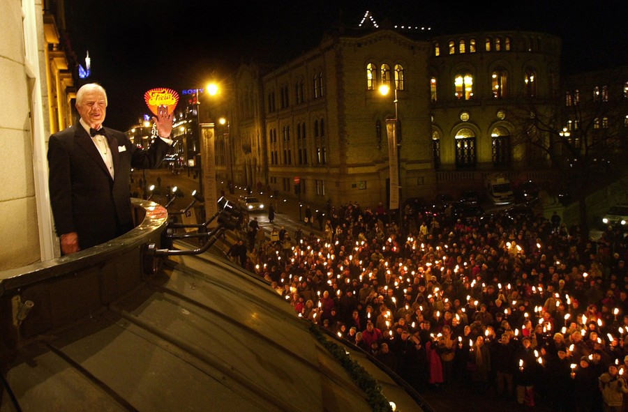 Jimmy Carter stands on a balcony, looking out at a crowd below who hold small torches.