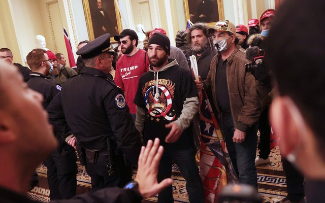 Insurrectionists inside the Capitol building, confronted by police. Man in center is wearing a QAnon T-shirt.
