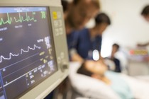 A monitor displays EKG readings while doctors attend a patient.