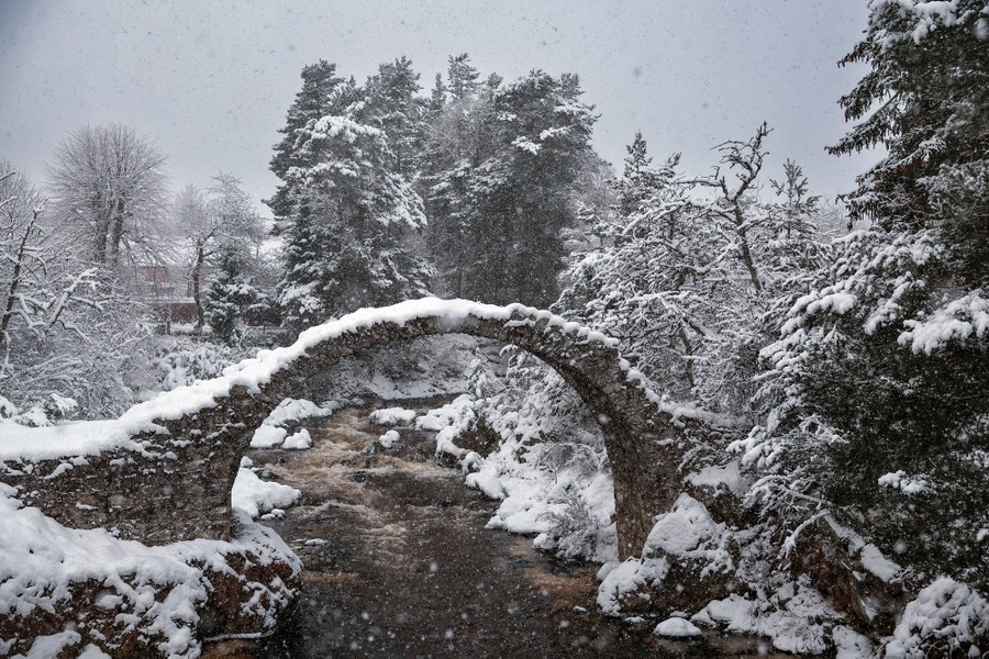 An ancient stone-arch bridge stands covered in snow.