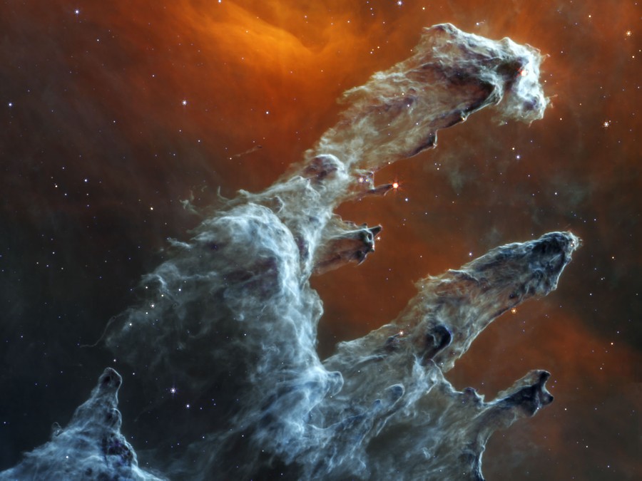 Dark clouds of gas and dust form pillar-like shapes against a glowing backdrop.