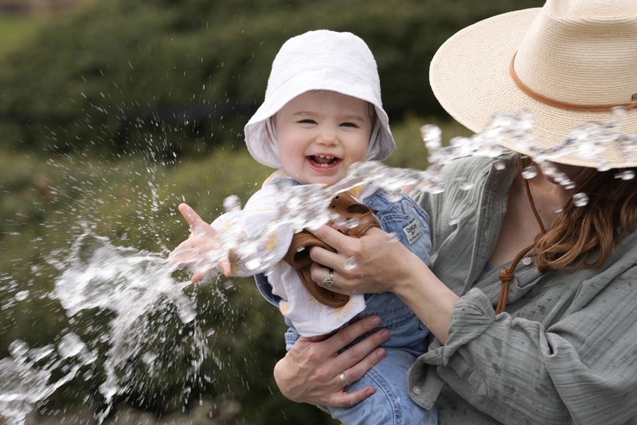 A child is held by her mother, playing with a water spray.