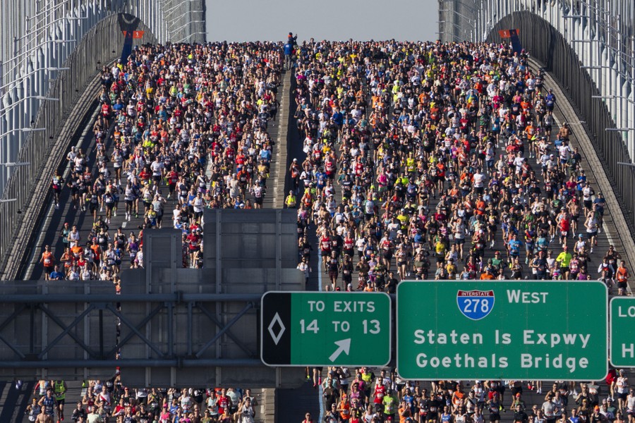 A distant view of hundreds of runners crossing a wide road bridge