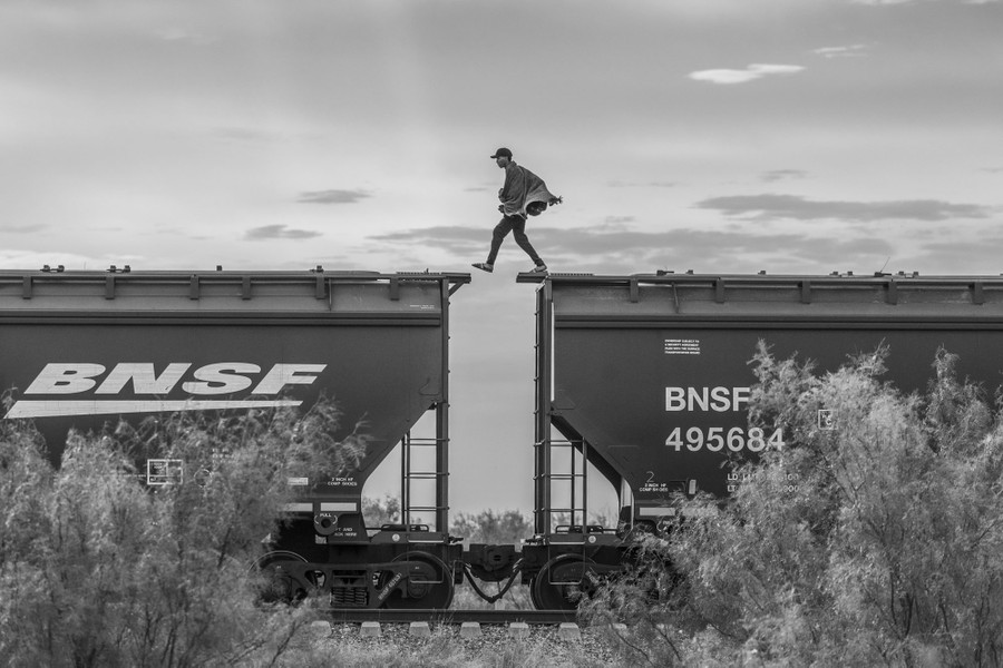 A person steps across the gap between two rail freight cars, while walking on top of them.