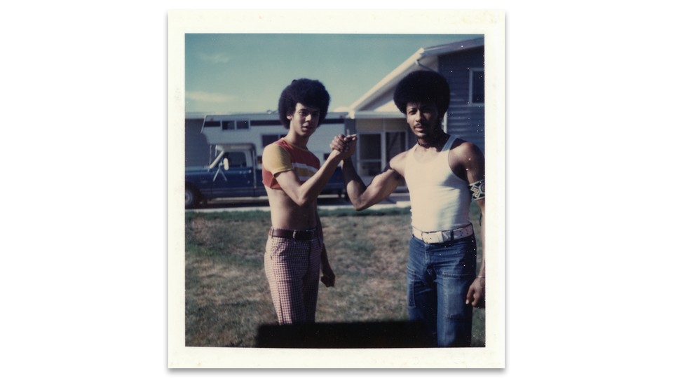 A polaroid of two people facing the camera, wearing casual clothing and afros, with their palms clasped together.