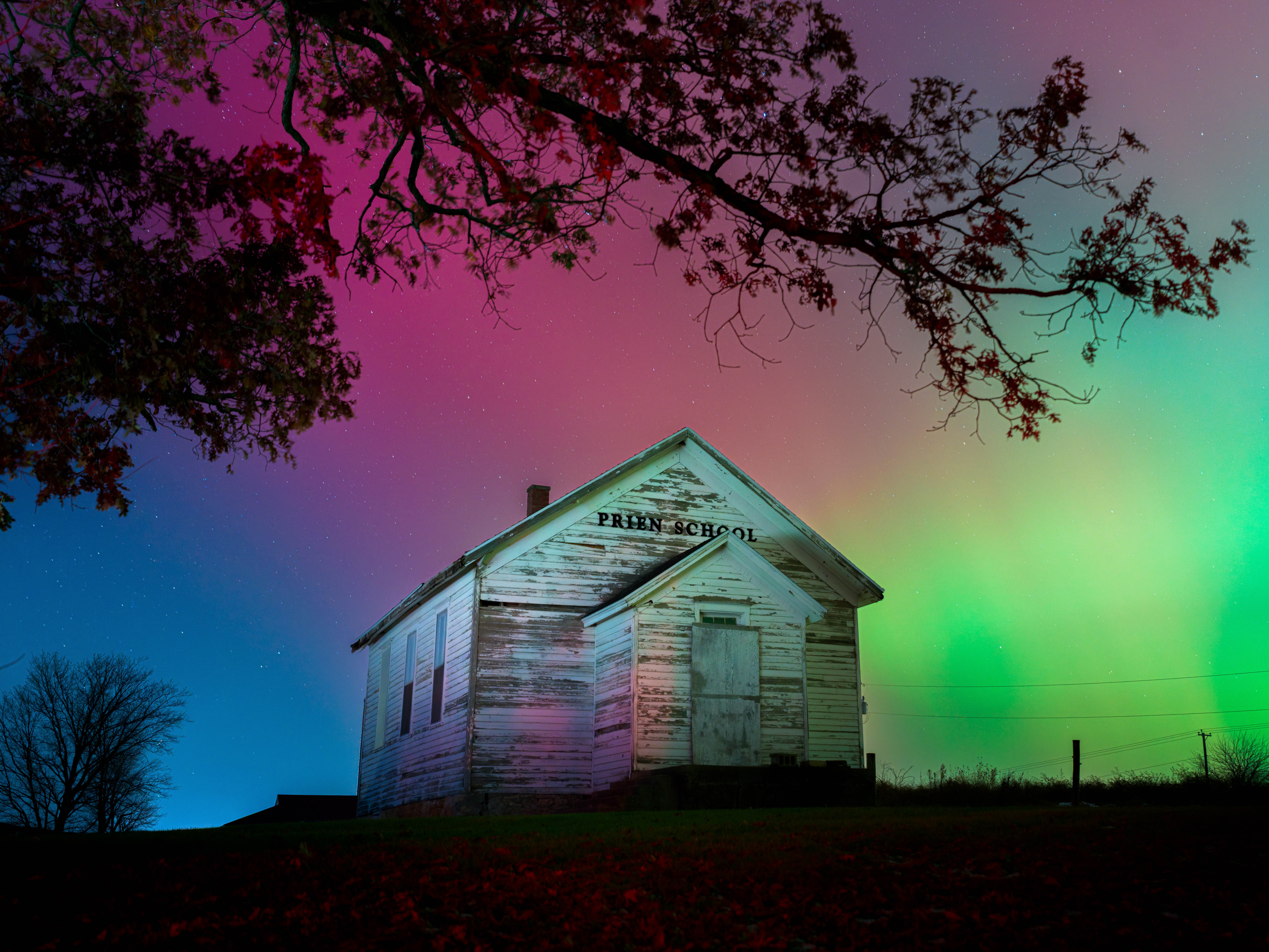 The night sky above a boarded-up wooden school house glows red and green.