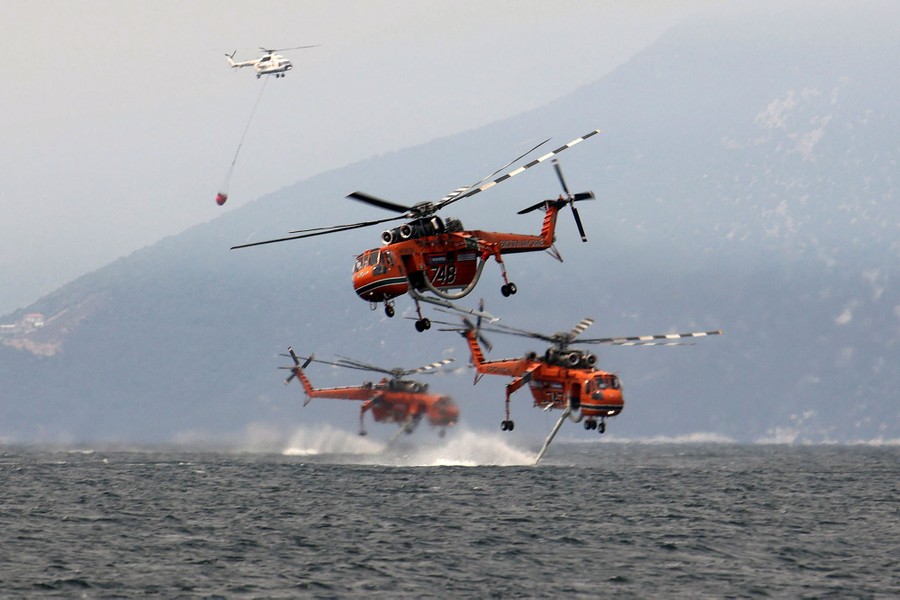 Several firefighting helicopters fly low and fill up with water of a beach.