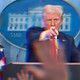 A blurred color photograph of Donald Trump in a White House press conference, pointing forward over a podium.