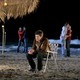 Seth Cohen sits alone on a beach chair while couples canoodle in the background