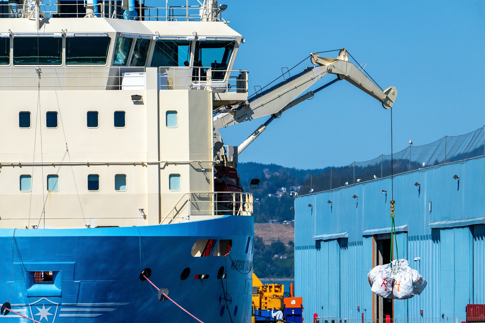 A ship uses a crane to offload bundles of plastic waste at a dock.