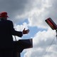 A photo of Trump speaking at a podium with the sky filling the frame