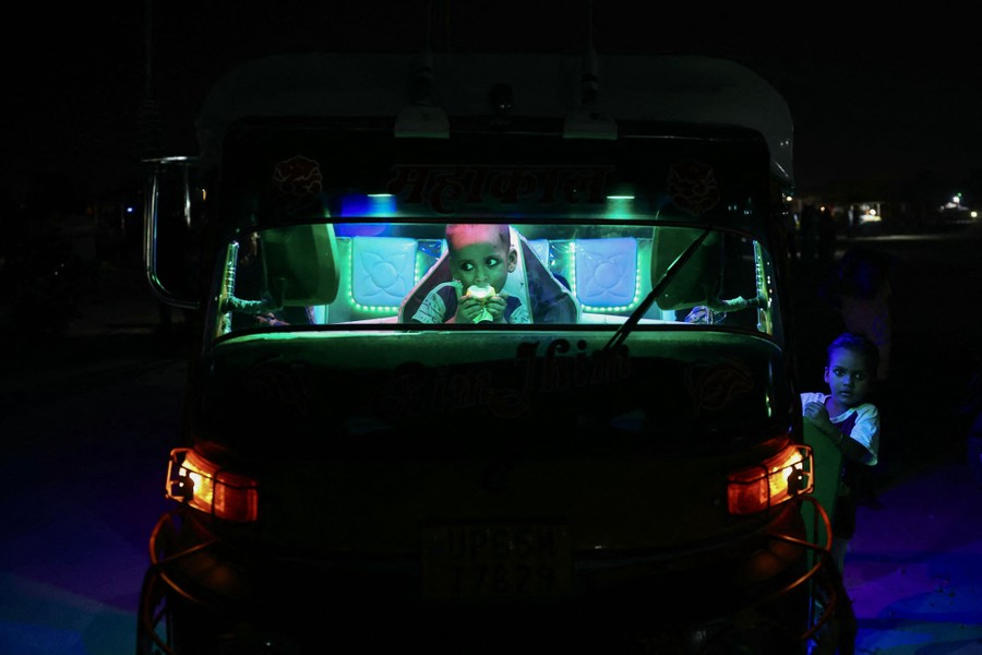 Two children sit in and beside an auto rickshaw at night.