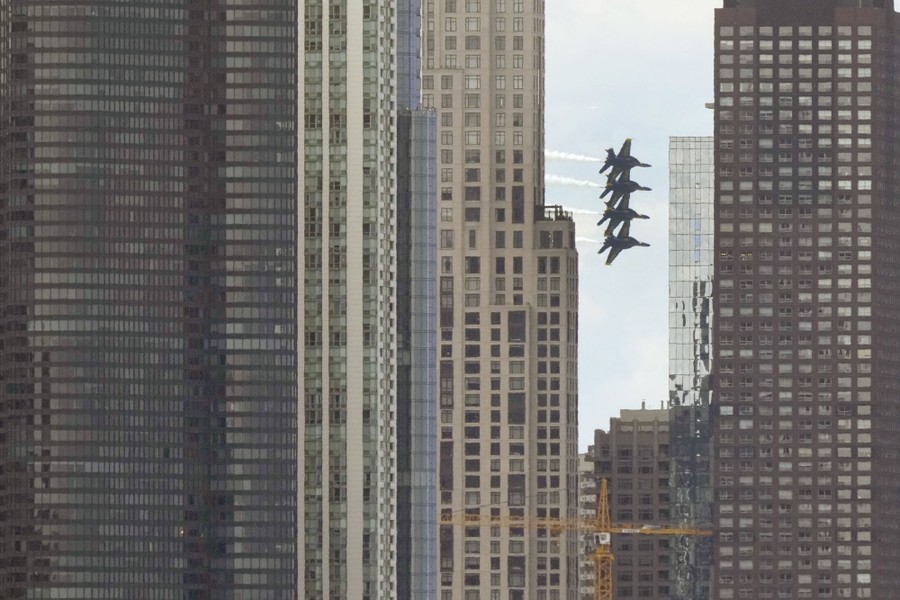Four fighter jets in the distance fly in a close formation, framed by tall buildings.