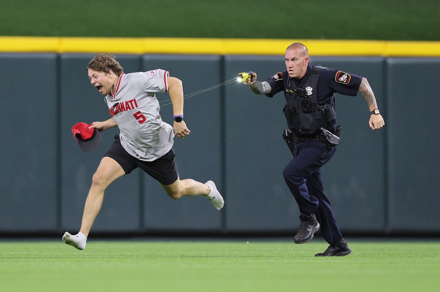 A baseball fan reacts while running across a baseball field, as they are tased by a police officer running close behind.