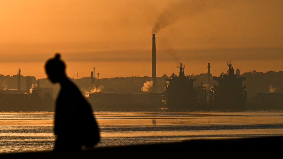 The silhouette of a person in front of a backdrop of an oil refinery in Havana, with an orange, smoky sky