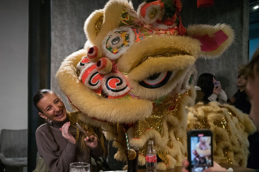 A person laughs in a restaurant as people in a large costume perform beside them.