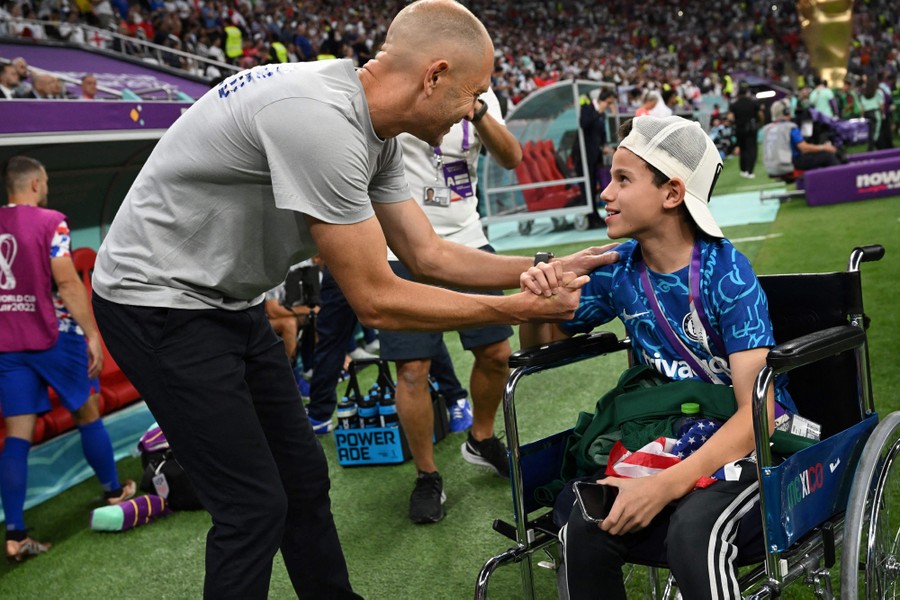 A soccer coach bends down to greet and shake hands with a young fan who is in a wheelchair.