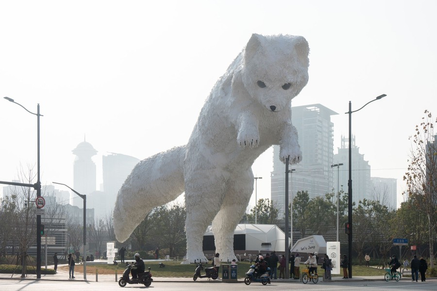 A very tall sculpture of an Arctic fox overlooks a city street.