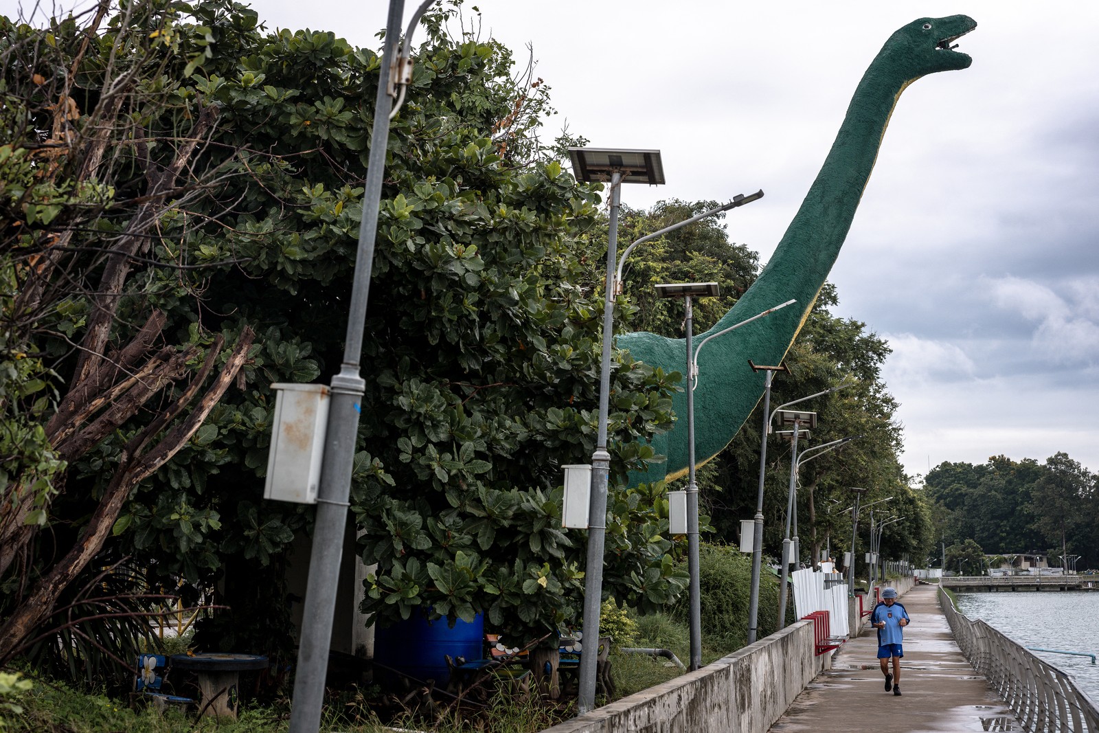 A man jogs past a tall dinosaur statue.