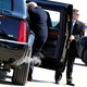 President Donald Trump climbs into a car held open by a secret service agent as exhaust comes out of the tailpipe.