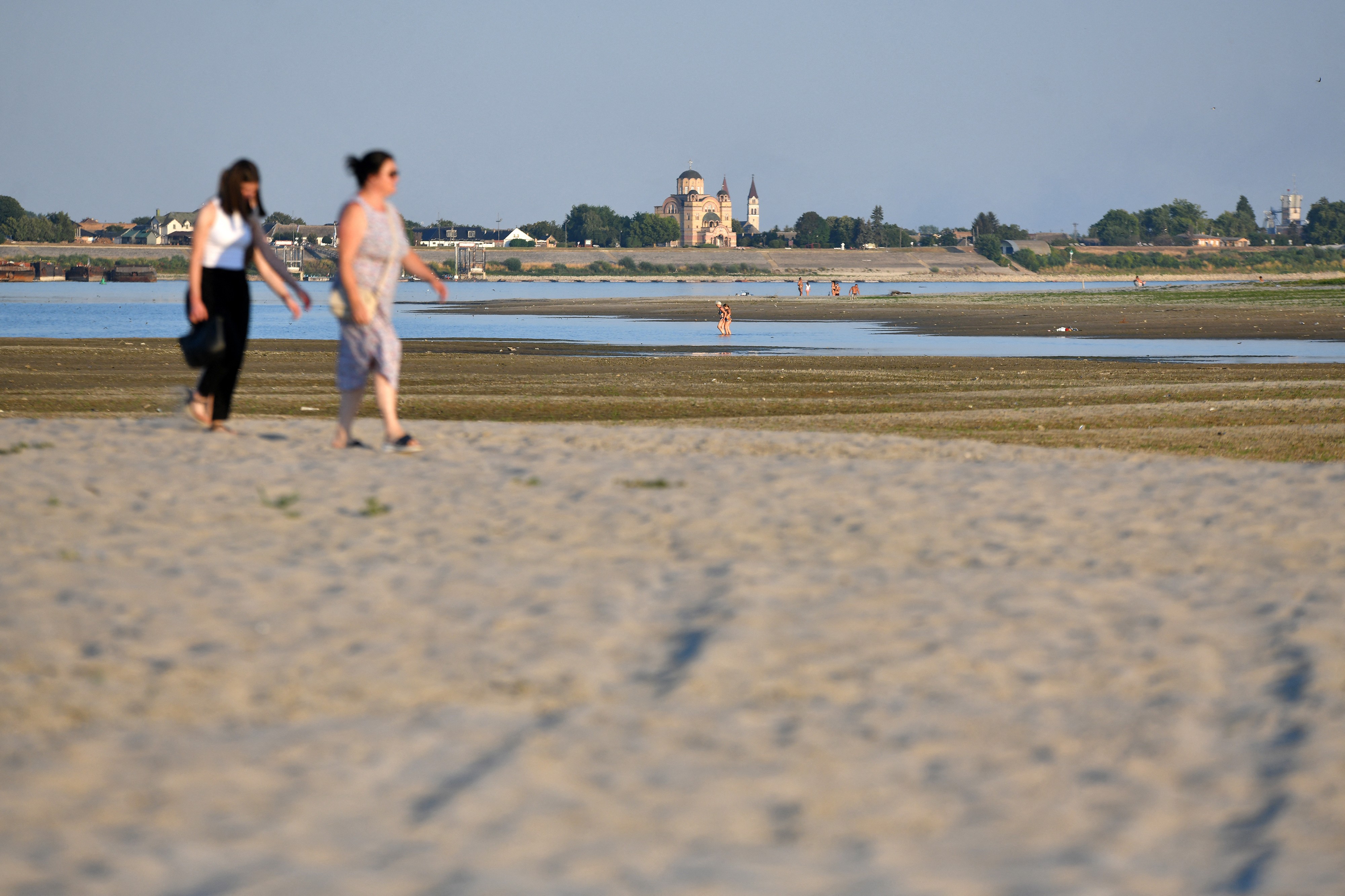 People walk across sandbars exposed by the low water level in a riverbed.
