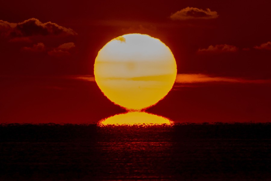 The sun rises against a red sky over a body of water.