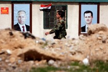 A Syrian government soldiers walks past rubble and posters of Bashar al-Assad and Vladimir Putin.