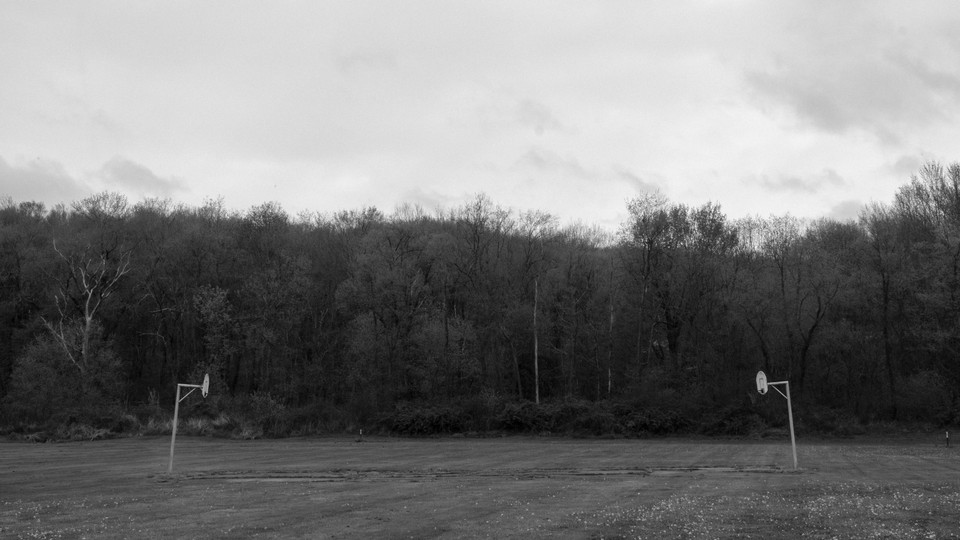 A black-and-white photo of two basketball hoops facing each other, and trees in the background