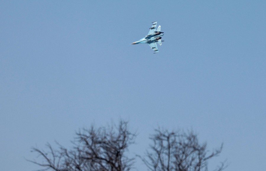 A fighter jet flies above a bare tree.