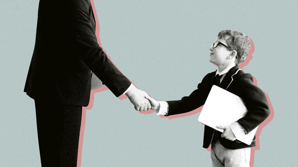 A child in a suit shakes hands with an adult businessman.