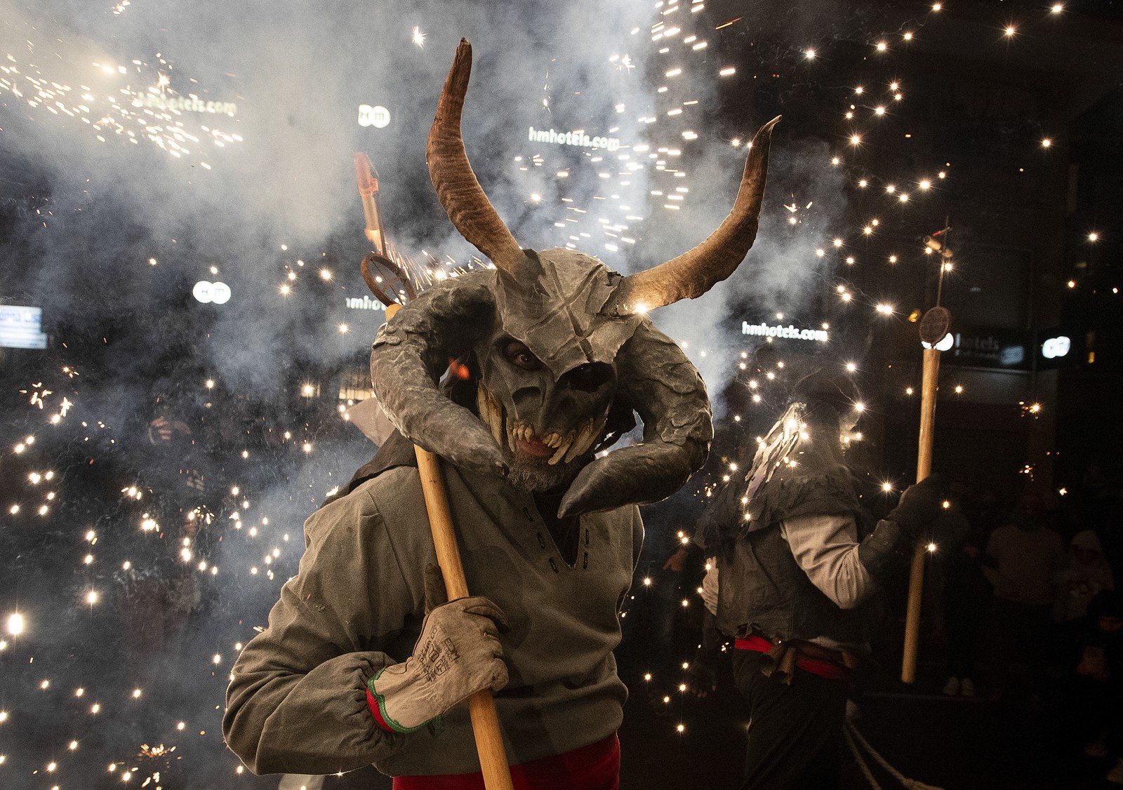 A parade participant dressed up as a demon carries a stick with fireworks.