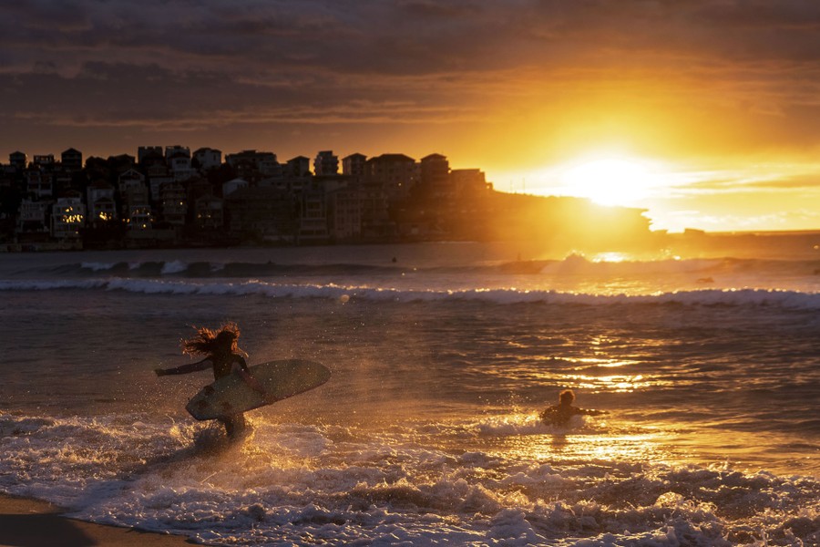 Two surfers run into the waves at a beach with the sun low in the sky.