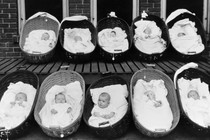 Ten babies, all but one sleeping, rest in baskets on a porch outside a maternity ward.