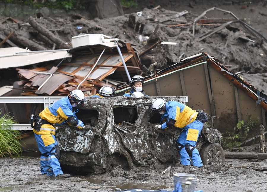 Police officers conduct search and rescue operation around a destroyed car.