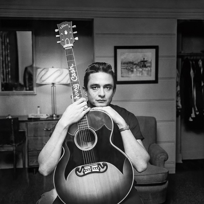 photo of Johnny Cash resting his chin on and holding a guitar with his name on the neck