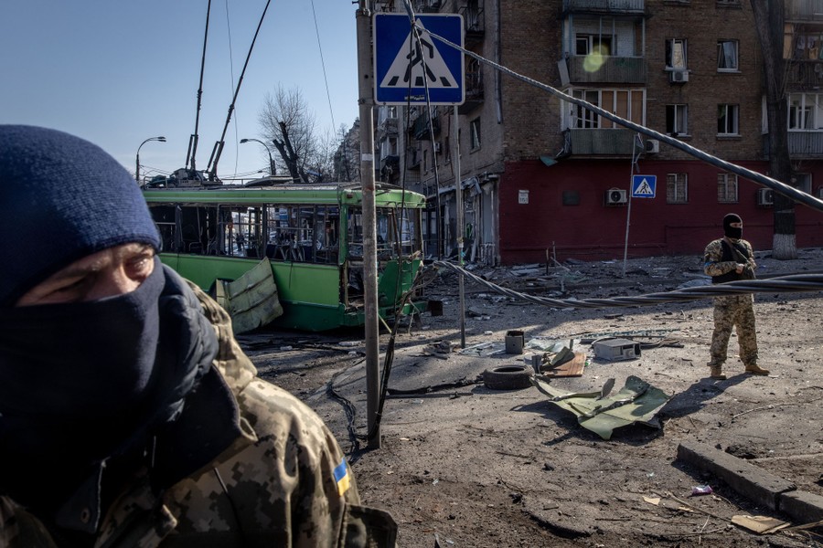 Several soldiers stand in a street strewn with debris, surrounded by damaged buildings and a tram.