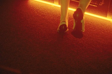 The back of a person's ankles as they walk away from the camera, wearing black heels with white stripes.