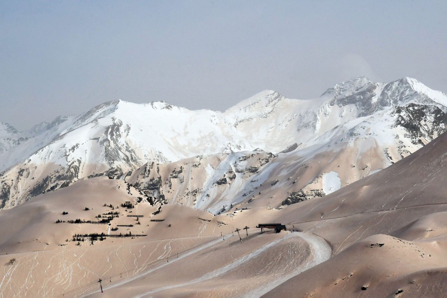 A view of snow-covered mountains—the lower elevations are lightly coated with sand.