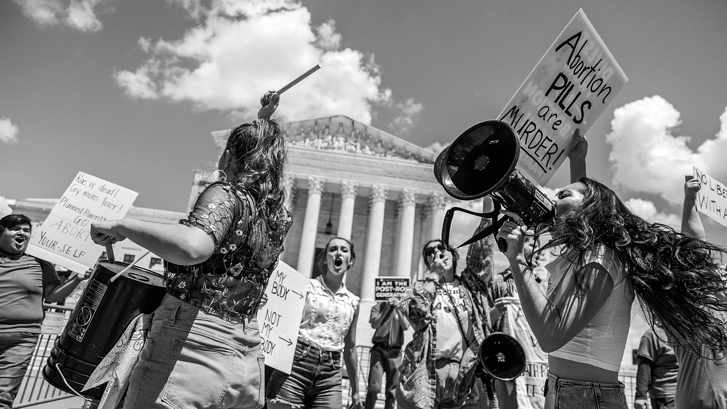 Fotografía en blanco y negro de manifestantes antiaborto tocando tambores y gritando con megáfonos frente a la Corte Suprema, sosteniendo carteles, incluyendo uno que dice, “¡Las PÍLDORAS abortivas son ASESINAS!”.