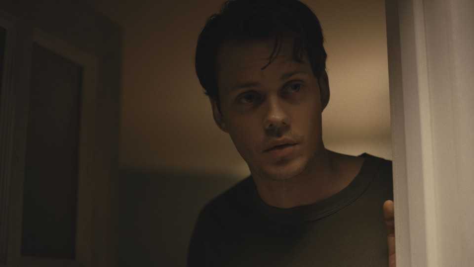 Bill Skarsgård peering around a door in "Barbarian"