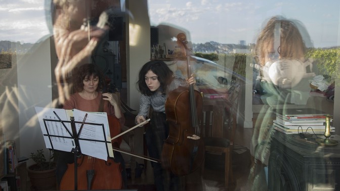Two women playing instruments inside as masked people watch