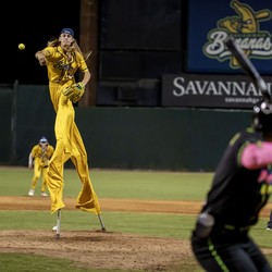 A baseball player wearing stilts pitches from a mound during a baseball game.