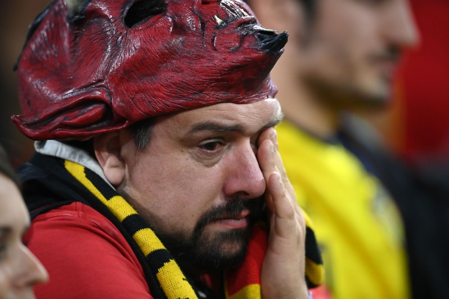 A sad man wearing a devil mask wipes his eyes.