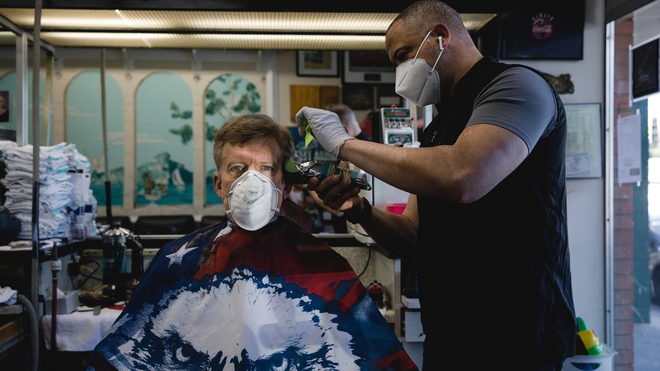 A stylist wearing a protective mask cuts a customer's hair at a barbershop in Atlanta.