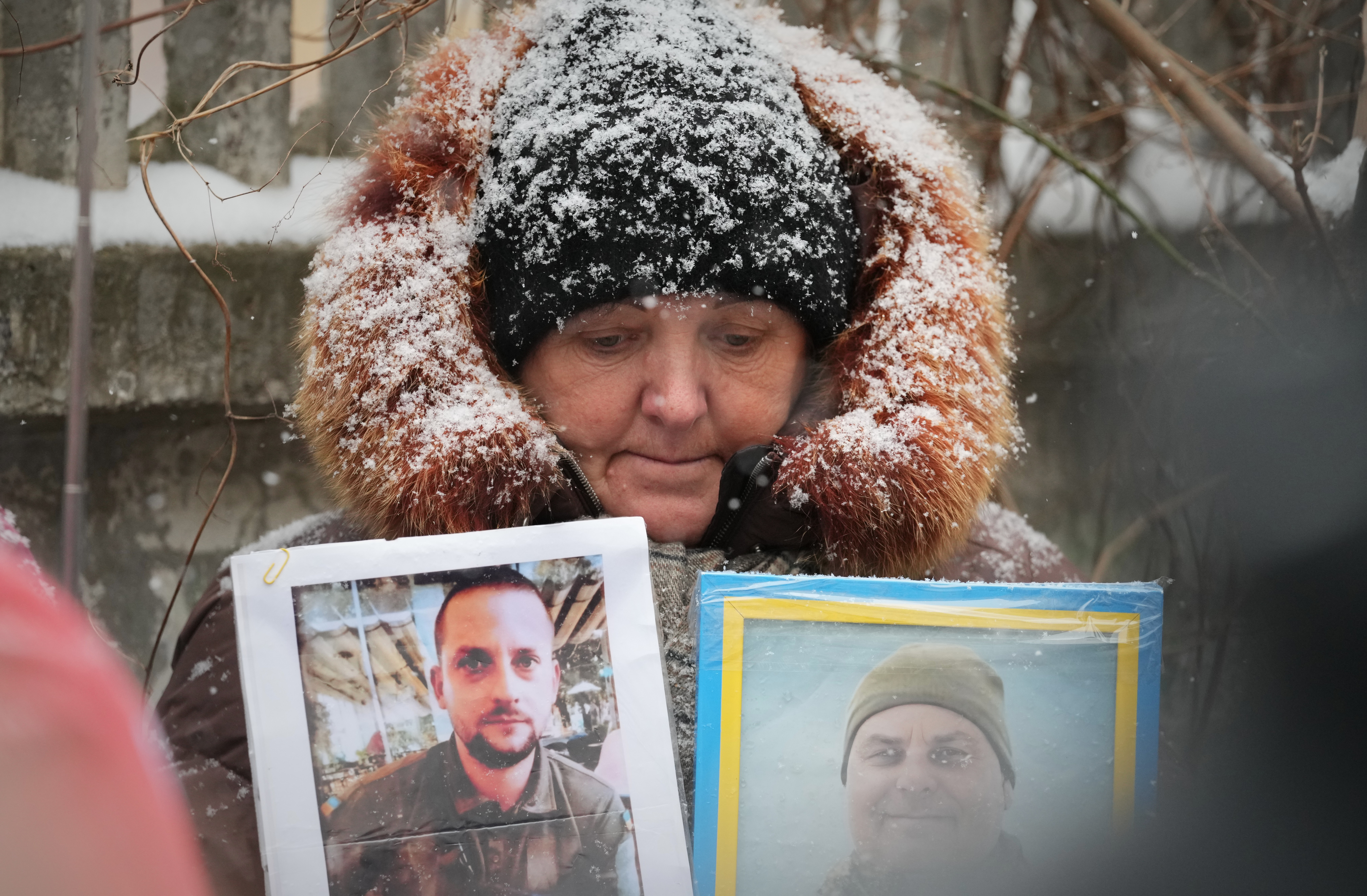 A woman, snow on her hat and hood, holds photos of her missing relatives.