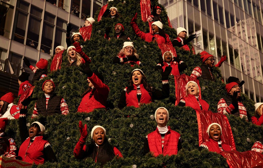 Singers in red vests stand in several tiers on a Christmas tree-shaped parade float.