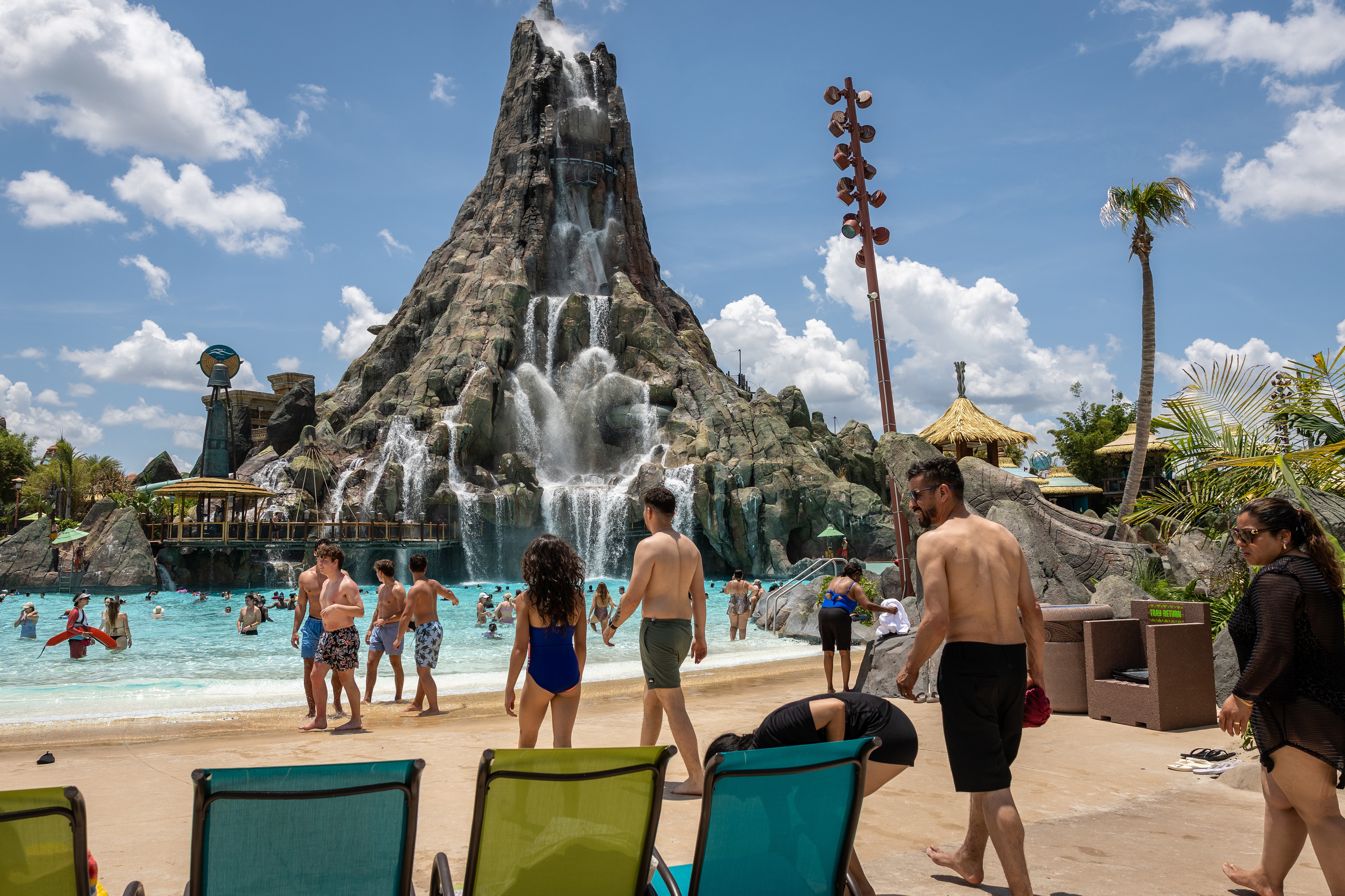People enjoy a water park with a tall volcano-shaped structure spewing water at center.