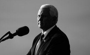 Mike Pence stands in front of a microphone, half in shadow.