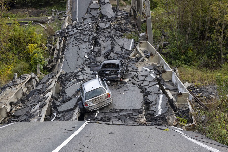 Two wrecked cars sit on the ruins of a collapsed road bridge.