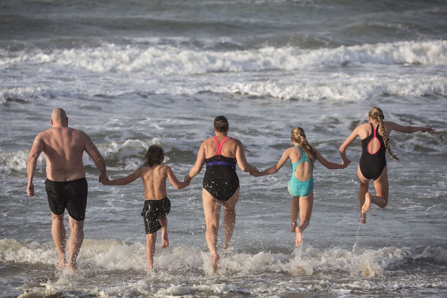 Five people hold hands as they run into the surf.